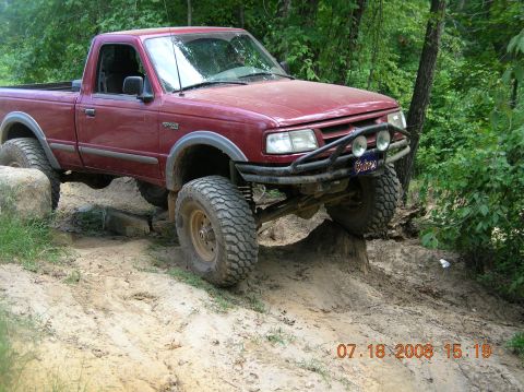 1991 Ford F-150 - This pickup truck is navigating a challenging off-road trail with large tires and a lifted suspension.