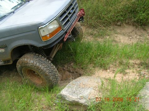1991 Ford F-150 - A 1991 Ford F-150 navigates a rocky, muddy off-road trail, with its front tire positioned on a large boulder.