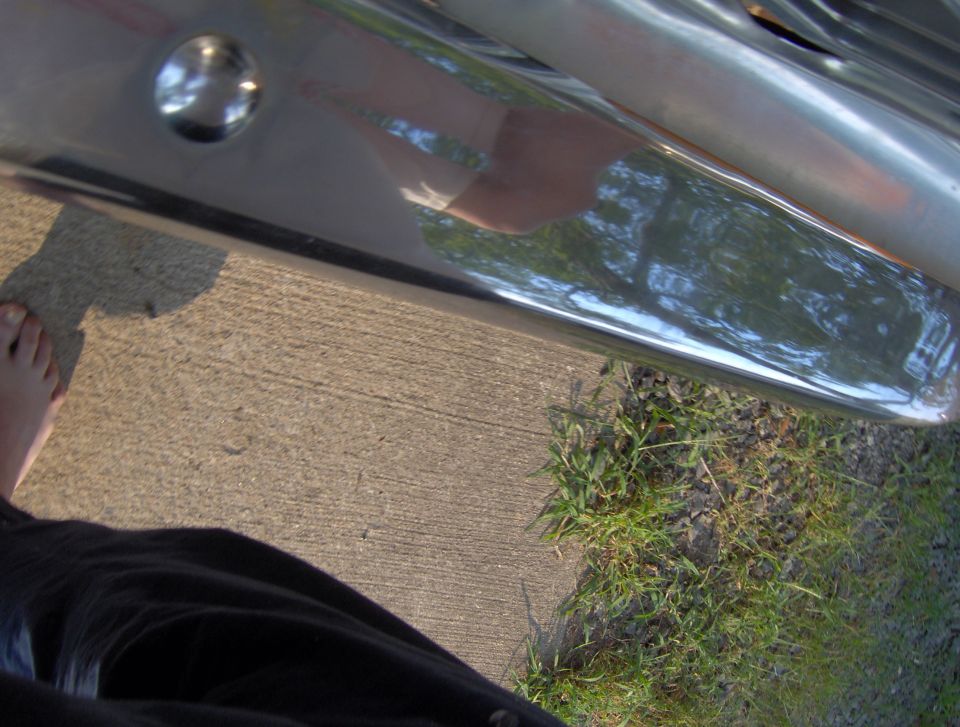 Chrome bumper with reflection of trees and a person's leg