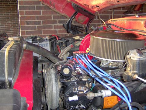 1978 Ford Bronco - Close-up view of a vehicle's engine bay, an open red hood, air filter, battery, and blue spark plug wires.