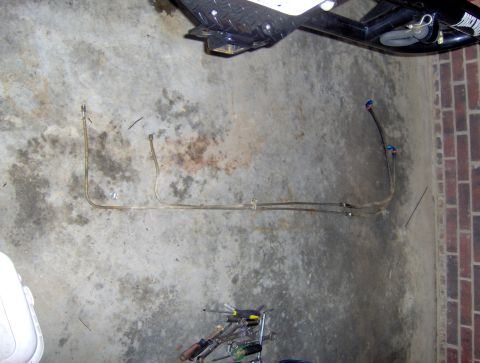 1978 Ford Bronco - Two metal fuel lines with blue connectors lie on a concrete floor next to a brick wall.