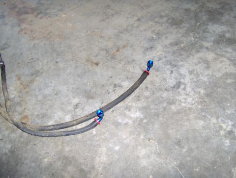 1978 Ford Bronco - Close-up of transmission lines with blue fittings and red bands, resting on a concrete surface.