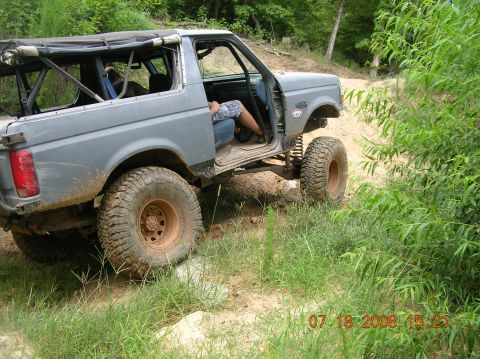 1991 Ford F-150 - A modified Ford Bronco navigates a muddy, overgrown trail with its doors removed.