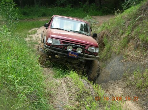 1991 Ford F-150 - A red truck with off-road modifications navigates a challenging muddy path.