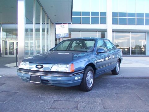 1998 Ford Taurus - A blue sedan, likely a 1986-1991 Ford Taurus, is parked outside a contemporary building.