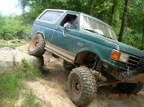 1991 Ford F-150 - This modified SUV is navigating a challenging off-road course with its tires on large rocks.