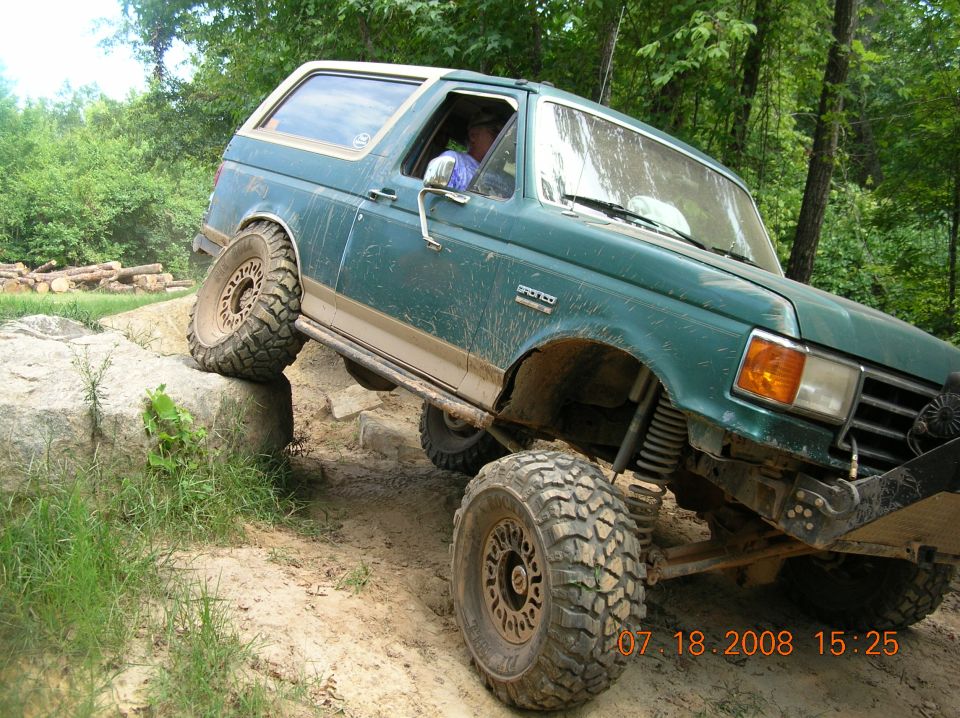 Green SUV with lifted suspension and large tires climbing rocks