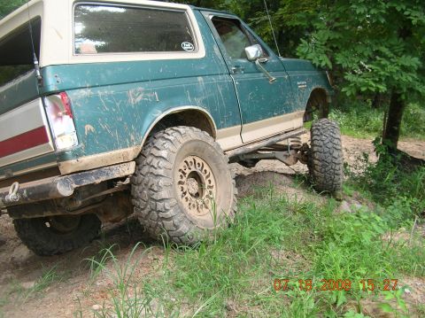 1991 Ford F-150 - This lifted Ford Bronco is shown off-road on a dirt path, covered in mud.