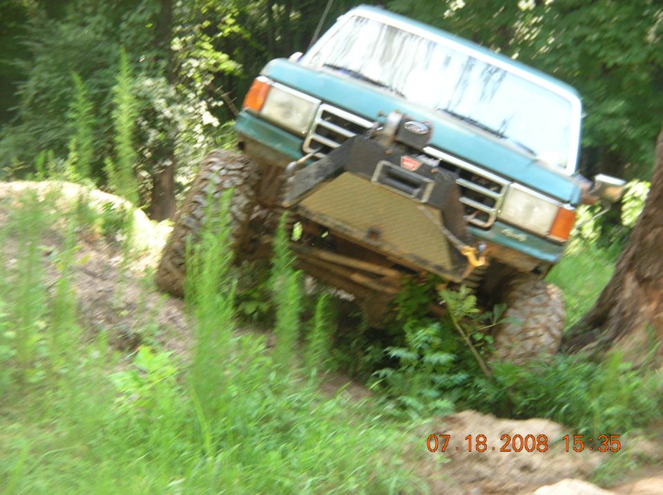 Teal Ford F-Series truck with large tires and winch on uneven terrain
