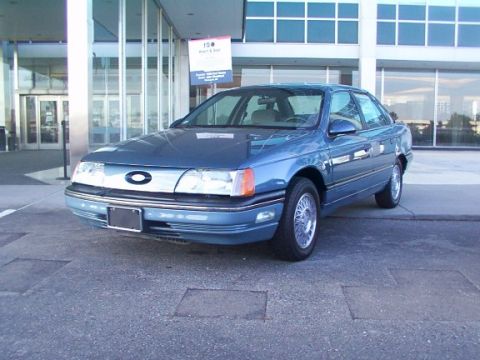 1998 Ford Taurus - A blue sedan is parked on asphalt in front of a building with large windows.