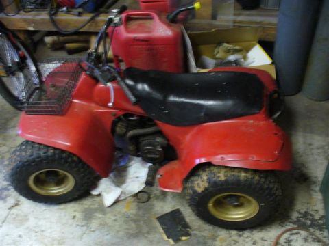 1988 Ford Bronco - A red all-terrain vehicle sits in a garage, with a red gas can mounted on the back.