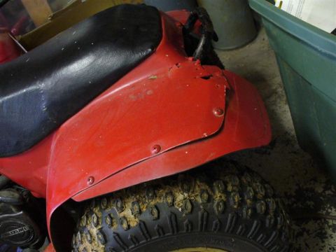 1988 Ford Bronco - Close-up of a red ATV's rear fender and a muddy tire. The Suzuki logo is visible on the engine casing.