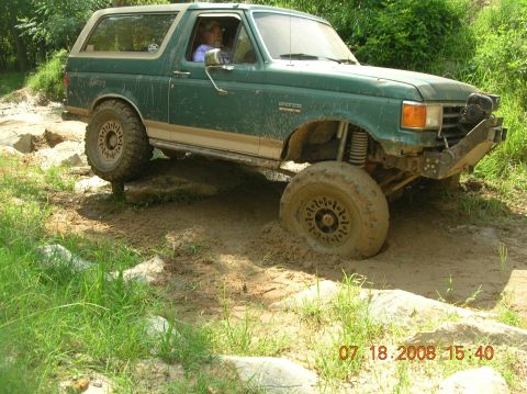 1991 Ford F-150 - Ford Bronco tackling a challenging off-road course with one wheel stuck in the mud.