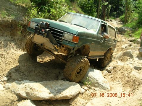 1991 Ford F-150 - This modified SUV is shown tackling a challenging off-road obstacle on a sunny day.