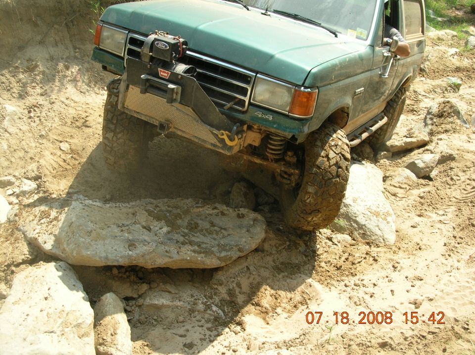 Green off-road truck with winch on front bumper navigating rocky terrain