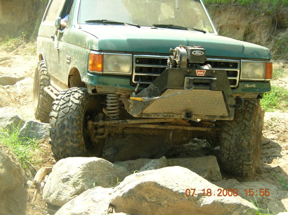 Green SUV with large tires and winch on front bumper navigating rocks