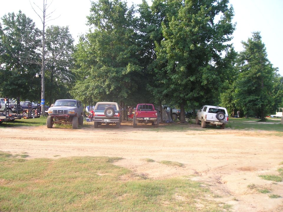 Lifted pickups and SUVs parked in a row at a dusty wooded off-road event