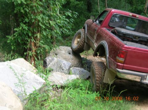 1991 Ford F-150 - A red pickup truck navigates a rocky off-road course, with one wheel lifted high.
