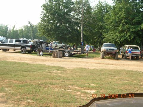 1991 Ford F-150 - Several trucks are parked on a dirt lot with trees in the background.