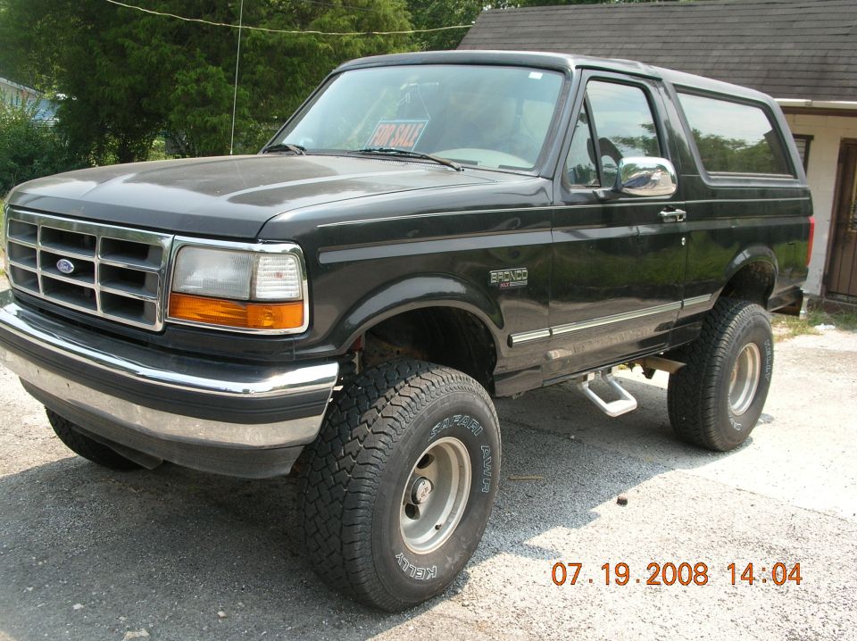 Black Ford Bronco with lifted suspension and off-road tires. 'For Sale' sign in window