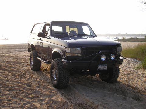 1995 Ford Bronco - This 1995 Ford Bronco is parked on a sandy beach near the water with boats visible in the distance.