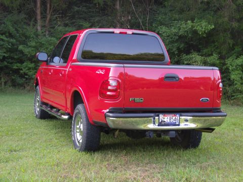 2007 Ford Mustang - This red Ford F-150 pickup truck is seen from the rear, parked on grass with trees in the background.