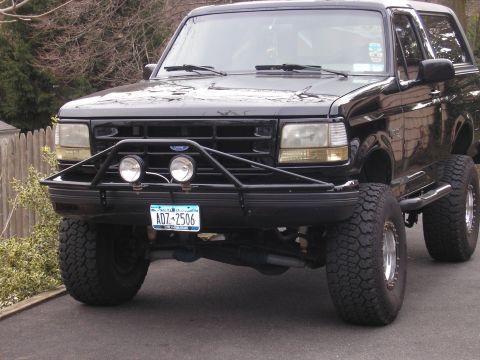 1995 Ford Bronco - This black Ford Bronco features a custom front bumper with auxiliary lights and large off-road tires.