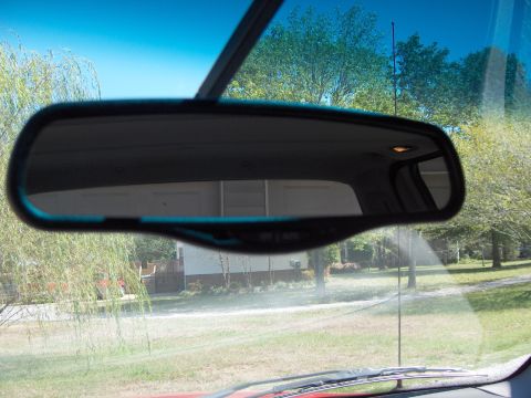 2007 Ford Mustang - View from inside a vehicle, looking at the rearview mirror which reflects a garage and the surrounding outdoor scenery.