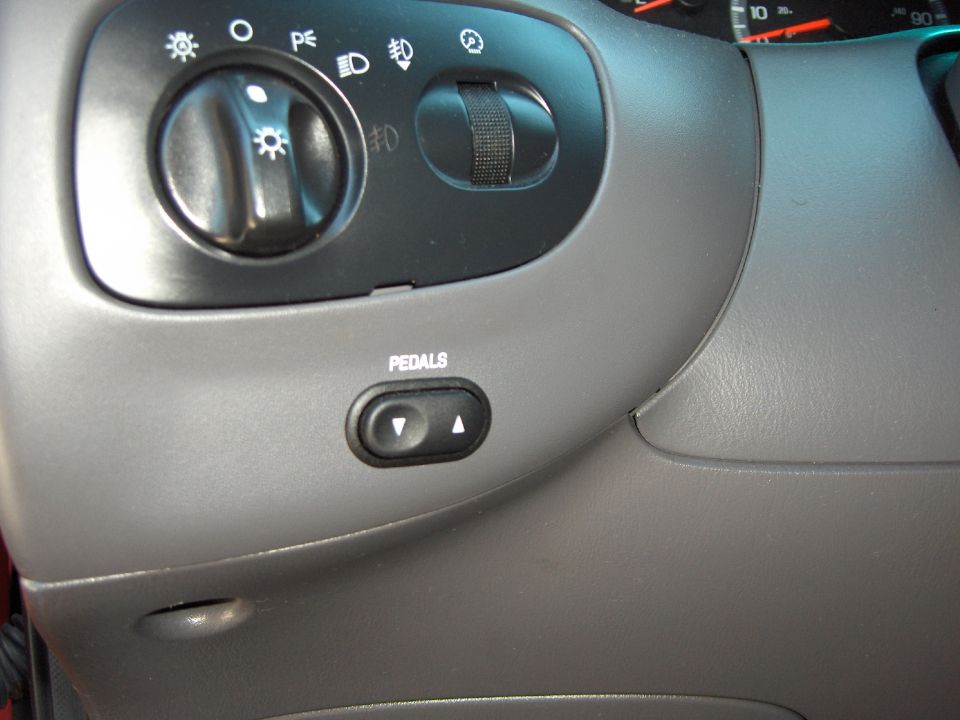Car interior showing headlight controls and power adjustable pedals button