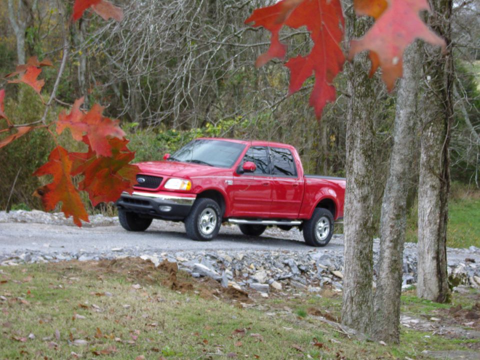 Red pickup truck parked on a gravel road, with autumn leaves in the foreground