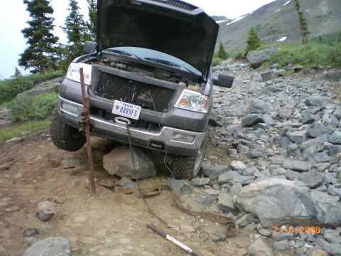 2004 Ford F-150 - A gray Ford F-150 is stuck on a rocky mountain trail with its hood open and a jack supporting it.