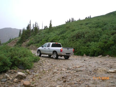 2004 Ford F-150 - Silver Dodge Ram pickup truck navigates a rough dirt road in a mountainous, wooded area.