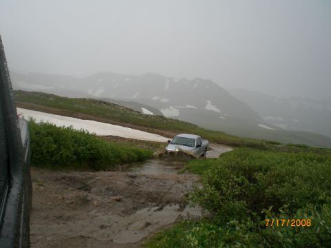 2004 Ford F-150 - Pickup truck navigating a muddy mountain trail with snow-capped peaks in the background.