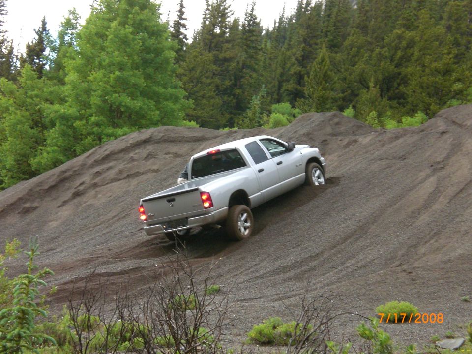 Silver pickup truck with a crew cab and long bed driving up a gravel hill