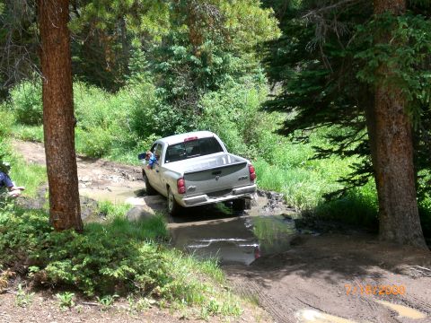 2004 Ford F-150 - A white pickup truck drives through a muddy obstacle on a wooded trail.