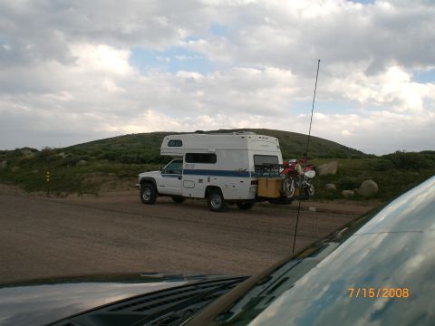 2004 Ford F-150 - A truck camper is parked on a dirt road with a motorcycle mounted on a rack at the rear.