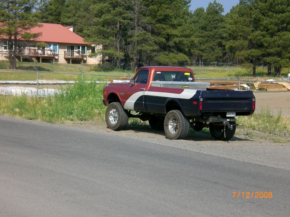 Red, white, and blue pickup truck with lifted suspension and chrome wheels parked on a roadside
