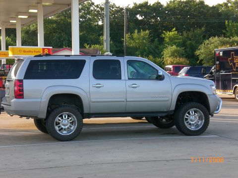 2004 Ford F-150 - A silver SUV with custom wheels and lifted suspension is parked at a gas station.