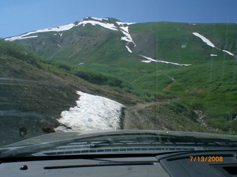 2004 Ford F-150 - View from inside a vehicle on a mountain road with snow and green hills under a bright blue sky.
