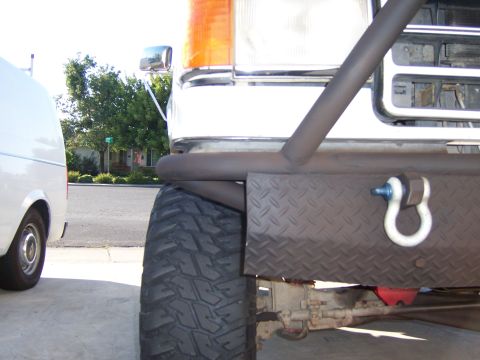 1991 Ford Bronco - Close-up of a custom front bumper with a tow shackle, parked next to a van.