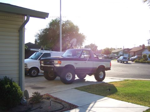 1991 Ford Bronco - This 1991 Ford Bronco features a custom front bumper and lifted suspension, parked next to a white van.