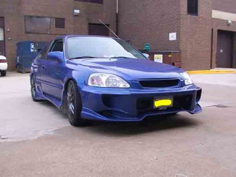1998 Ford Taurus - A modified blue coupe with an aggressive body kit is parked in front of a brick building.
