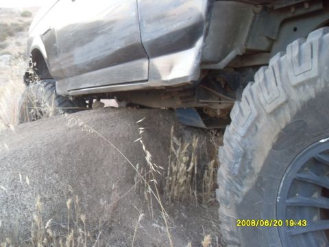 1990 Ford Bronco - A dark-colored SUV is positioned on a dirt mound with its large off-road tires visible. The vehicle appears to be navigating a rough terrai…