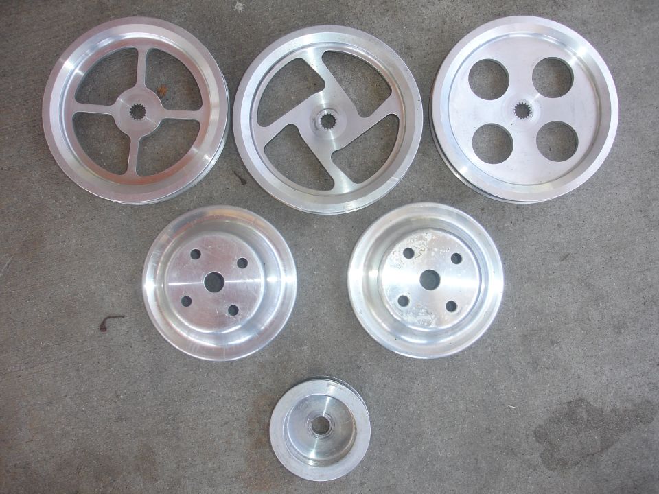 Six aluminum pulleys of different sizes and designs on a gray concrete surface.