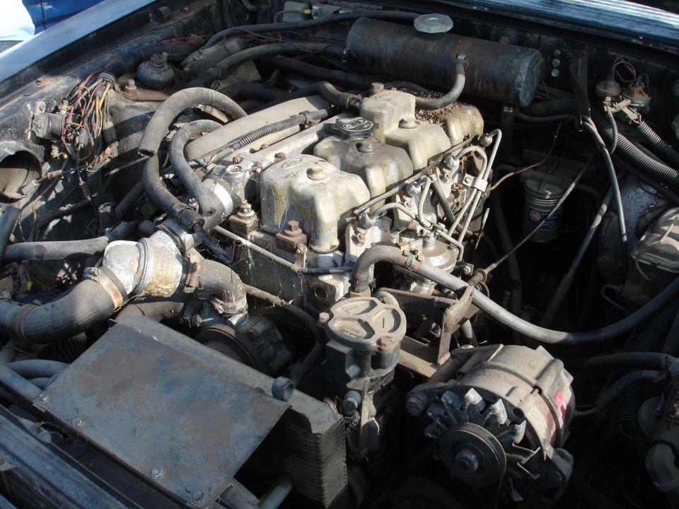 Close-up of a dirty V-engine in a vehicle, showing hoses, wires, and engine components.