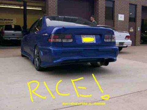 1998 Ford Taurus - A blue sedan is parked outside a building, with the word RICE! written in yellow on the ground.