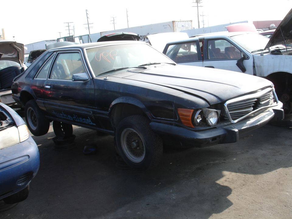 Dark blue coupe with "turbo diesel" text on the side in a junkyard.