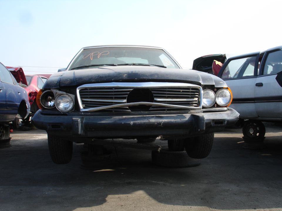 Front view of a dark sedan in a junkyard.