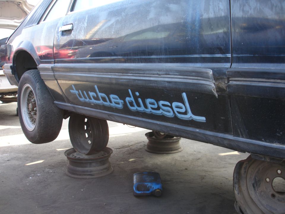 Dark sedan side view, lifted on jack stands, with visible text on the door