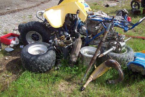 1989 Ford Bronco II - A yellow ATV is in pieces on the grass, with various parts scattered around it.